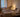 Adult resting in soft neutral bedding beside a bedside fan in a calm European bedroom, lit by warm evening light and a peaceful summer mood.