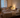 Adult resting in soft neutral bedding beside a bedside fan in a calm European bedroom, lit by warm evening light and a peaceful summer mood.