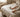 Close-up of hands neatly stitching a small tear in a light duvet cover on a made bed in a soft, neutral European bedroom.